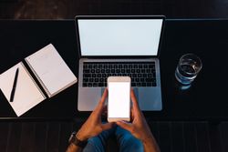 Anonymous man browsing smartphone near laptop