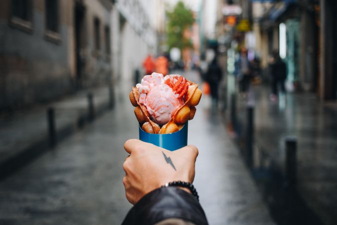 Tattooed hand holding waffle and ice cream dessert, landscape