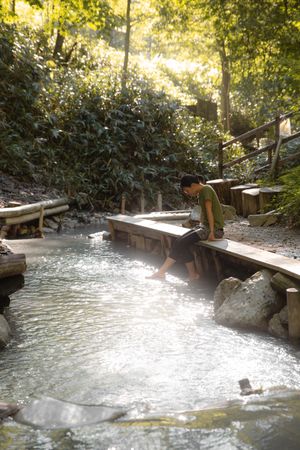 Woman in green shirt sitting on brown wooden dock by the river