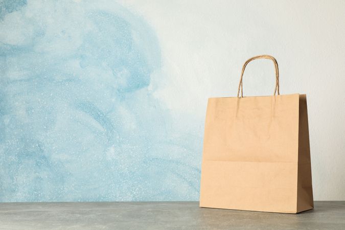 Paper bag on grey table against blue background, copy space