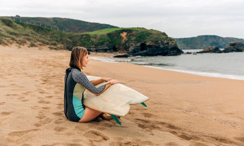 Woman sitting on the shore with surfboard gazing at the ocean