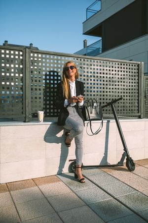 Happy businesswoman using mobile with her scooter next