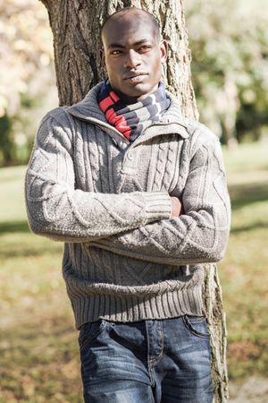Serious male in woolen sweater standing in front of trees in park