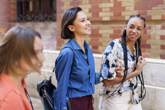 Women talking while walking next to brick wall