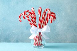 Candy canes in glass jar on blue background, space for text