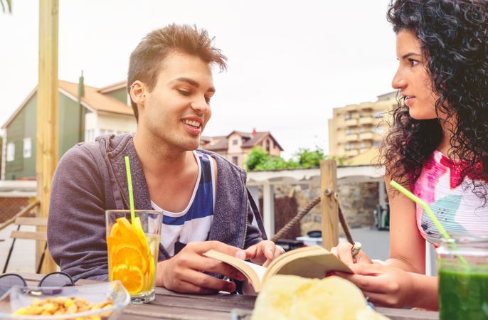 Friends talking with cocktails and open book on outside table