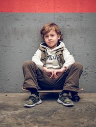 Cool child sitting on skateboard near wall