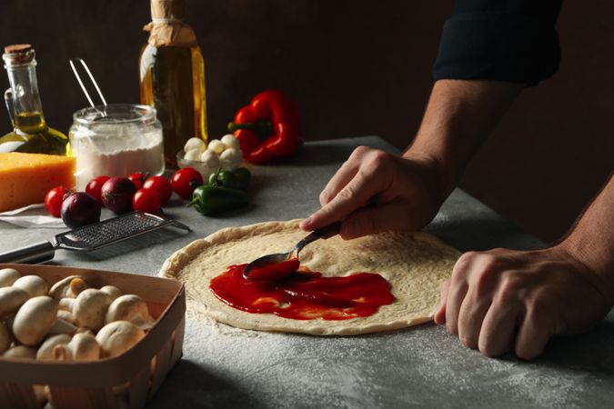 Man cooking pizza on gray table with ingredients