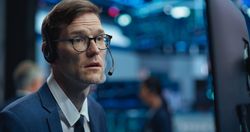Adult Man in Glasses Looking at Computer Screen, Communicating with a Client on a Phone Call, Talking About a Buying Strategy
