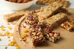 Tray with granola bars and bowl with almond on wooden background