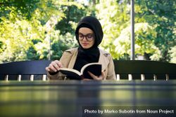 Woman reading a novel at a park table on a sunny day 0VYM3b