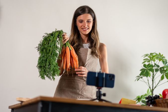 Woman holding fresh carrots while filming a healthy cooking tutorial