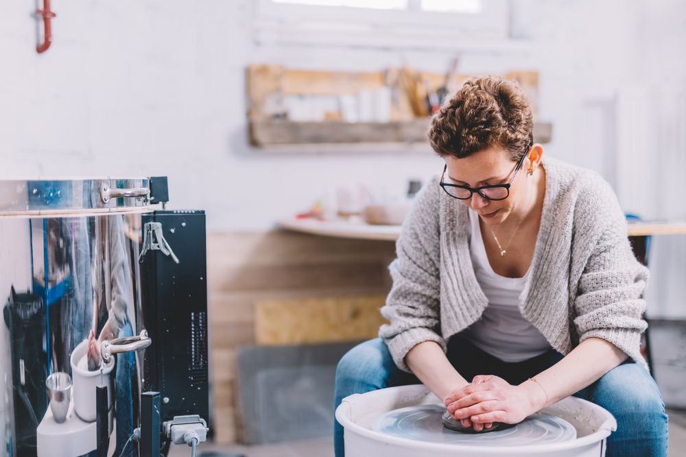 Woman potter shaping vessel on wheel