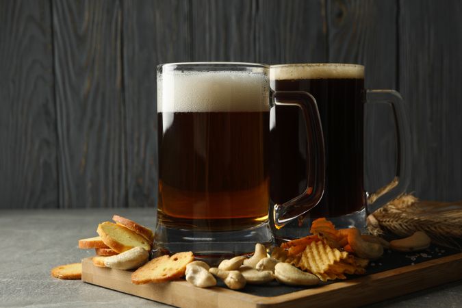 Beer and snacks on gray table against wooden background
