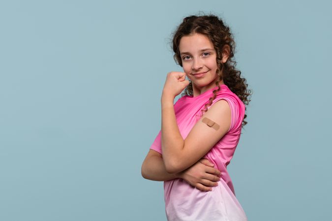 Confident girl flexing arm, showing bandage after vaccination.