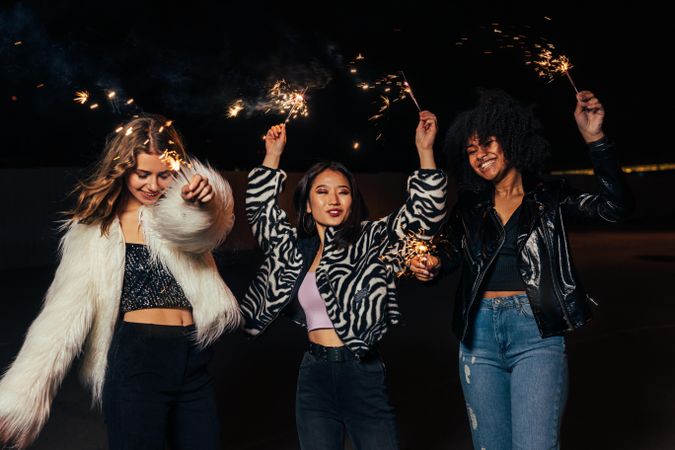 Three female friends laughing and  smiling with sparklers at night