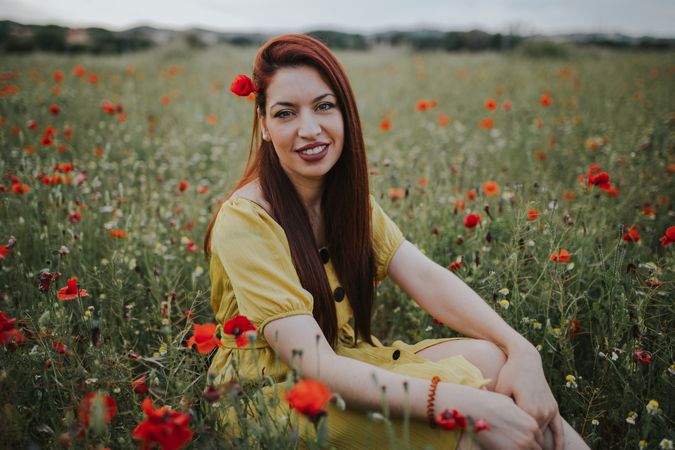 Woman sitting in field with poppies and daisies