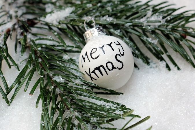 Merry Xmas on a light bauble beside pine tree leaves