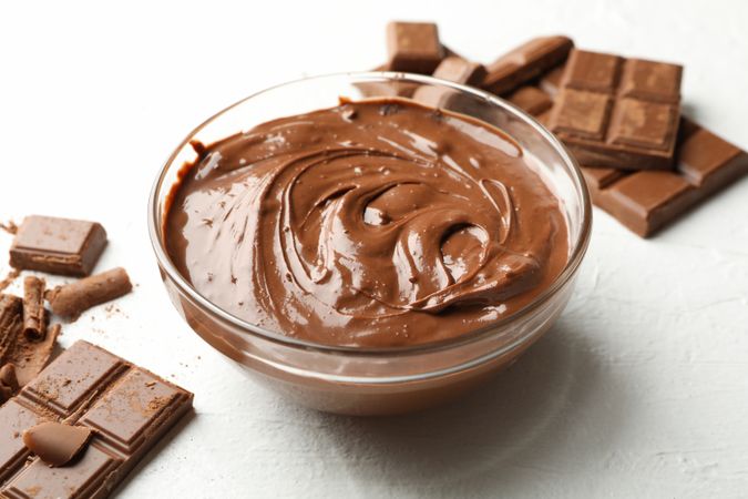 Bowl with chocolate and chocolate pieces on neutral background