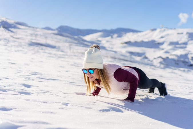 Female in snowsuit doing plank on snowy mountain