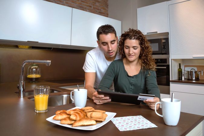 Couple paying for something over breakfast with credit card on tablet