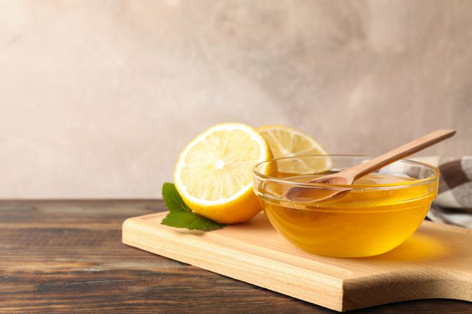 Lemons and bowl with honey and dipper on wooden background, space for text