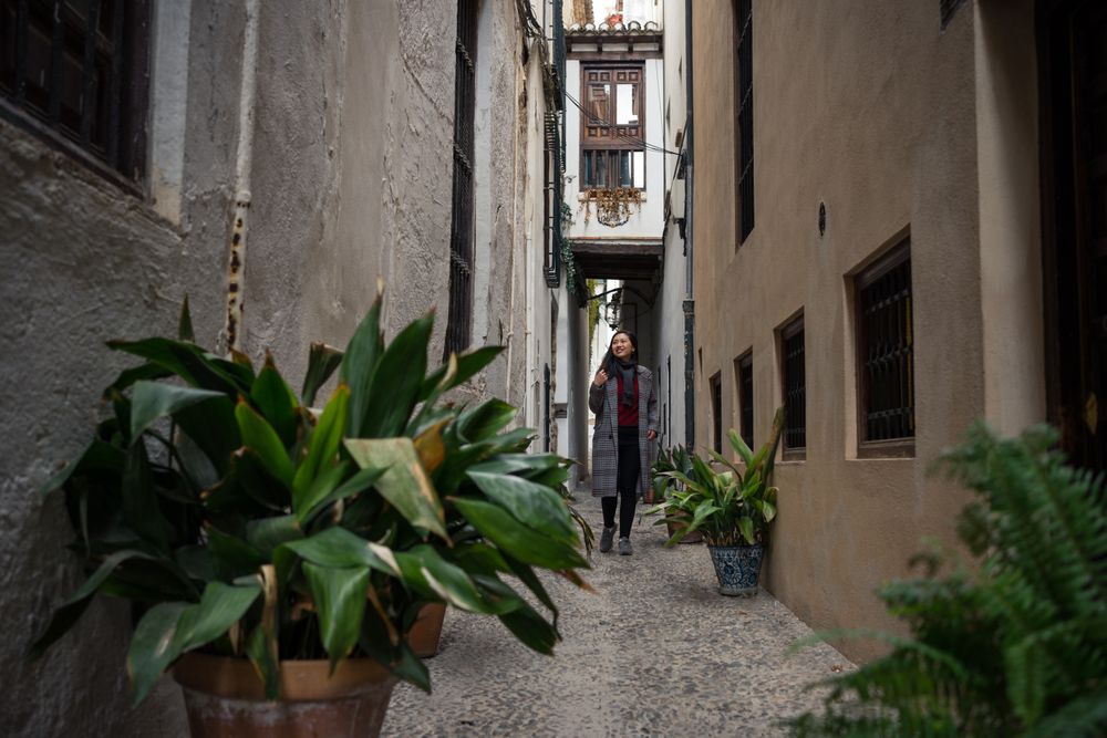 Female traveler in casual clothing at alley with quick pot of flowers