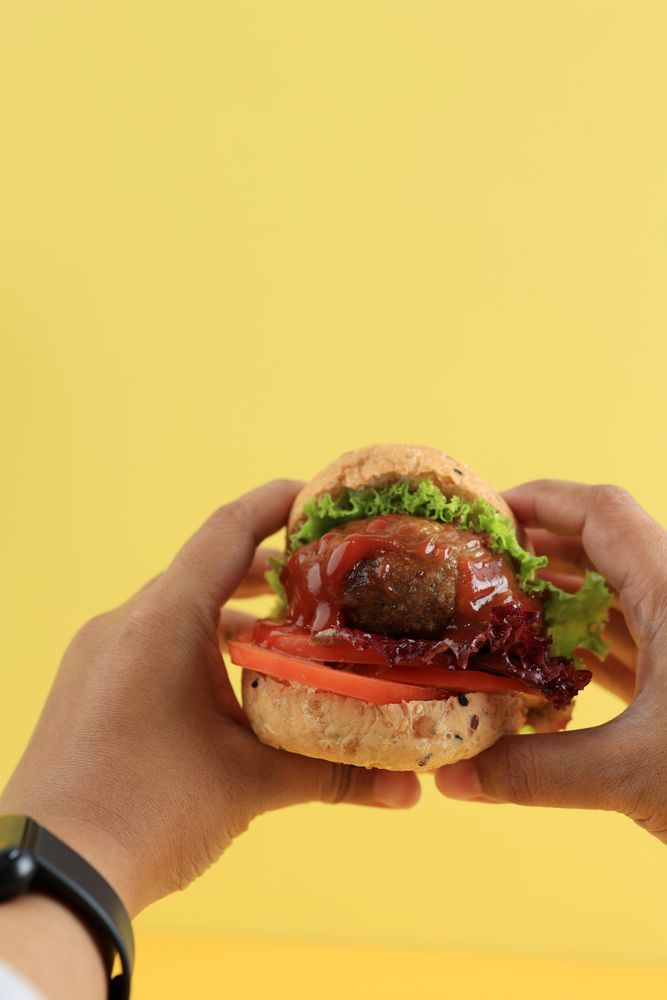 Female Hand Holding Mini Beef Burger with Lettuce and Tomato