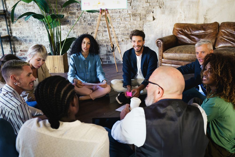 A multi-ethnic creative marketing team of creatives sitting on the floor gathered together for brainstorming session