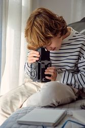 Boy with aged photo camera on bed at home