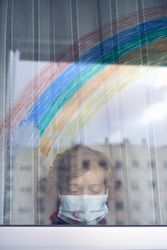 Boy in medical mask standing near window