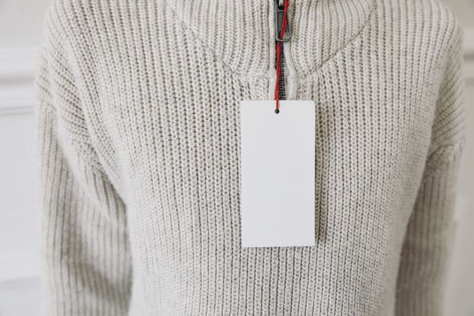 Blank paper price tag, label mockup on beige knitted sweater