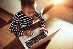 Girl concentrates while working on laptop in sunny kitchen