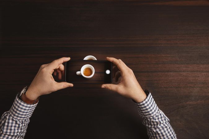 Top view of man wearing plaid shirt taking picture of espresso shot with cell phone