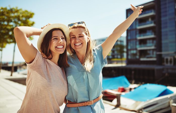 Two women laughing together with arms up on sunny day next to the river