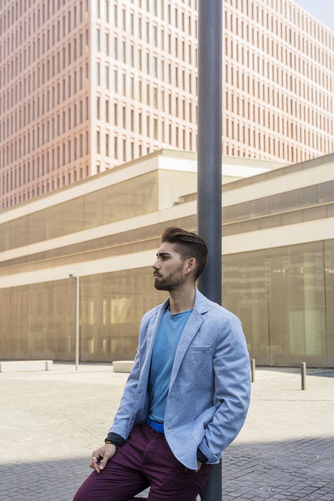 Man in blazer leaning on pole with one hand in pocket
