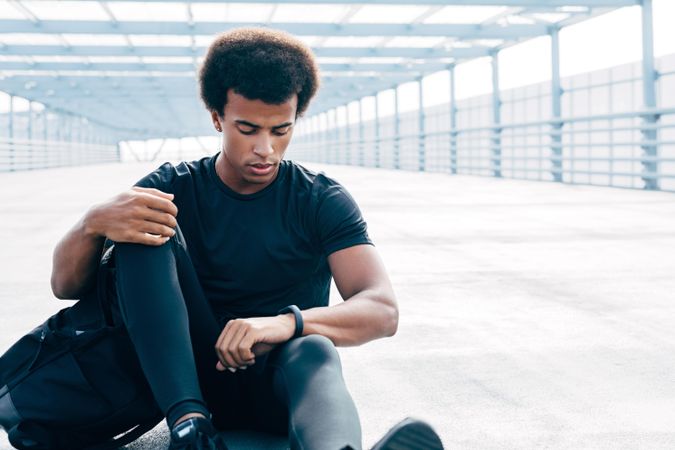 Black man sitting on bridge checking smart watch after training