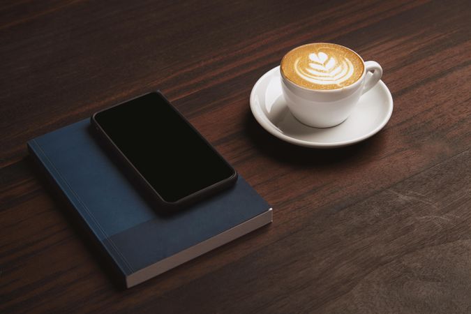 Cappuccino, cell phone and navy notebook on wooden table