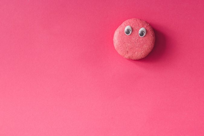 French macaron with googly eyes bright pink background