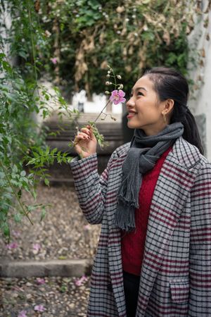 Young female in casual clothing touching green plants and smiling at rocked lane