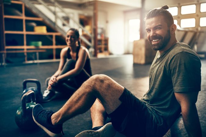 Two smiling people sitting on gym floor