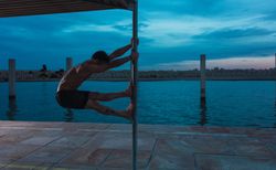 Athletic man balancing on pole on embankment