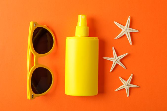 Composition with sunscreen spray, starfishes and sunglasses on color background, closeup. Summer backdrop