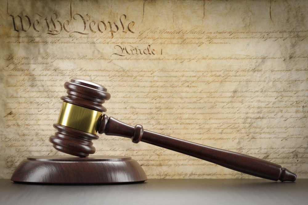 United States Constitution On Wall with Gavel Resting on Table in Front.