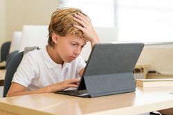 Tired boy using tablet during lesson at school