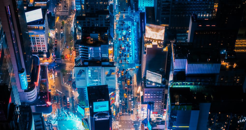 Night Aerial Shot of New York City with Skyscraper Spires and Straight Busy Streets with Cars and Yellow Taxi Vehicles. Top Down Helicopter View of Office Buildings in a Big Urban Center