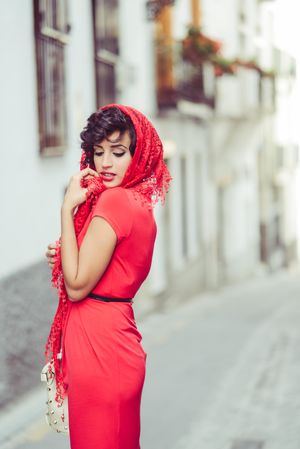 Elegant woman in dress holding onto her lace scarf in pedestrian street