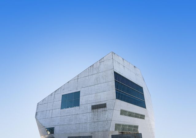 Grey modern building with unsymmetrical windows with blue sky