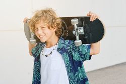 Cheerful boy with skateboard on neck