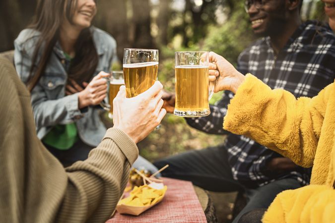 Happy multi-ethnic group of friends gather outside to chat and have a beer together
